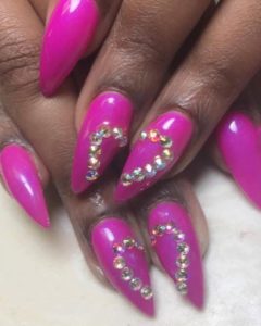 Image of pointed nails painted pink with rhinestone hearts spanning the middle and ring fingers.